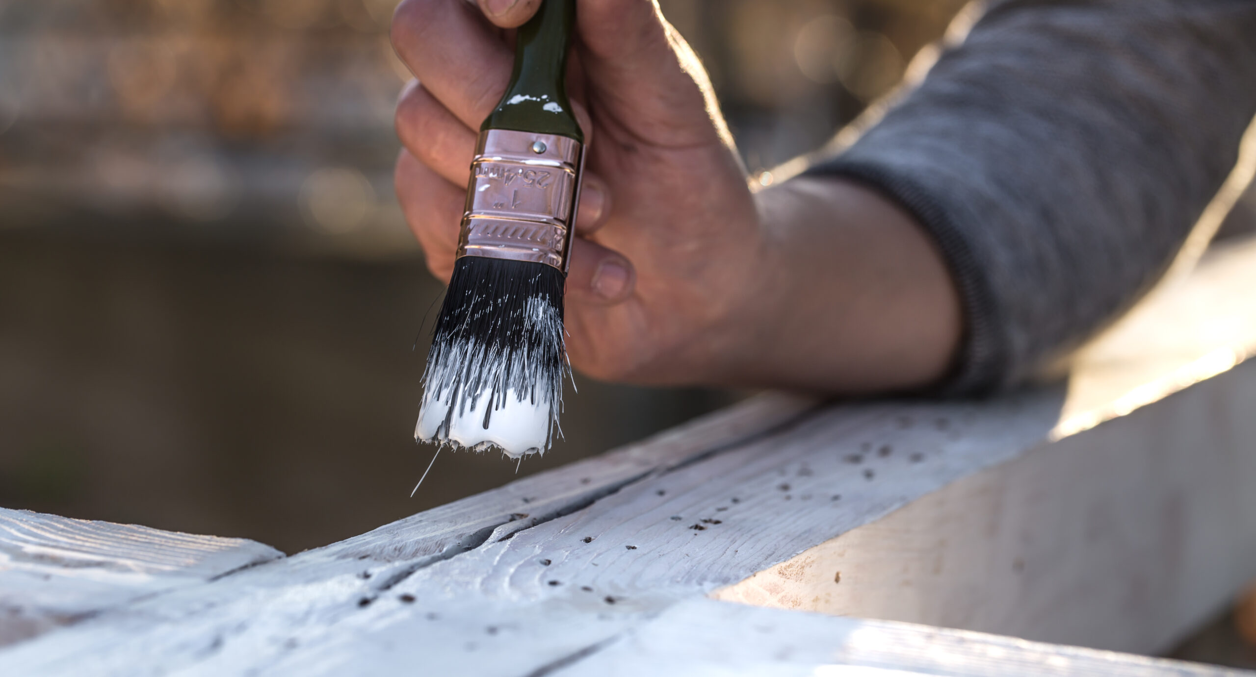 male hand paints with white paint on wood